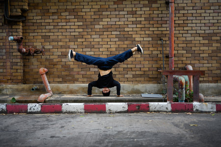 Generation Z male hip hop dancer doing cartwheel against brick wall in the city.