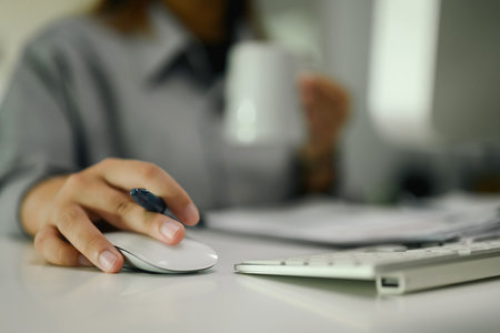 Close up of female office worker using computer mouse on desk.