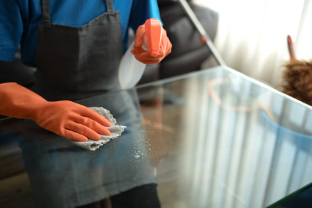 Millennial woman wearing gloves wiping dust and cleaning glass table in living room.の写真素材