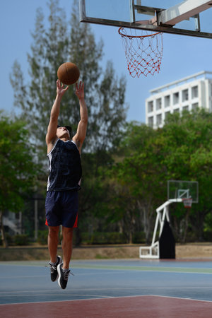 Athletic male training outdoor, playing basketball on sports court.
