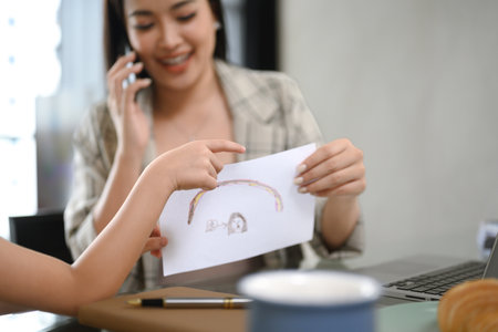 Young mother trying to work at home with her little daughter wanting attention.の写真素材