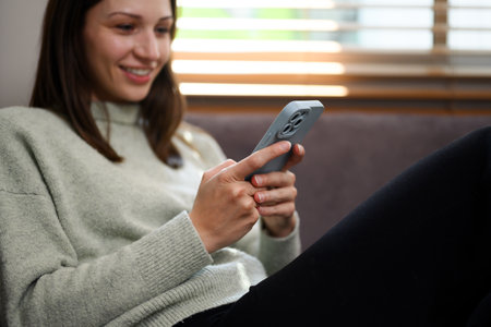 Happy caucasian woman relaxing on couch and using mobile phone.の写真素材