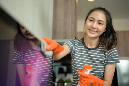 Pretty young woman wearing rubber gloves cleaning oven with rag in kitchen.の写真素材