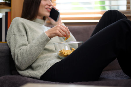 Happy young woman eating cookies and chatting with friends on phone.