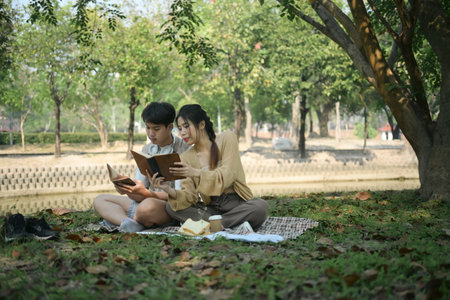 Relaxed young couple spending time together outdoor reading book on picnic blanket in the park.の写真素材