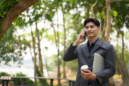 Smiling businessman having pleased phone conversation outside on a sunny day.の写真素材