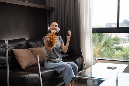 Cheerful young woman having fun cleaning house, singing and using duster as microphone.