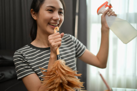 Cheerful young housewife singing, using duster as microphone while cleaning house.の写真素材