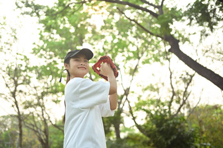 Joyful asian girl in leather glove playing baseball on green grassy lawn during summer day.の写真素材
