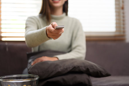 Young woman with remote control watching television on sofa at home