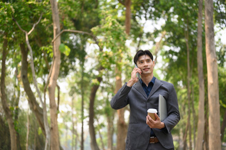 Handsome young businessman talking on mobile phone while standing at urban park.の写真素材