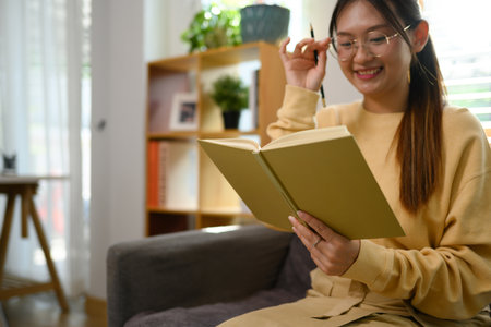 Pretty young woman listening to music with headphone and reading book at home.の写真素材