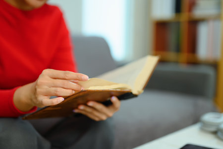 Closeup young woman in warm sweater reading book on couch at home.