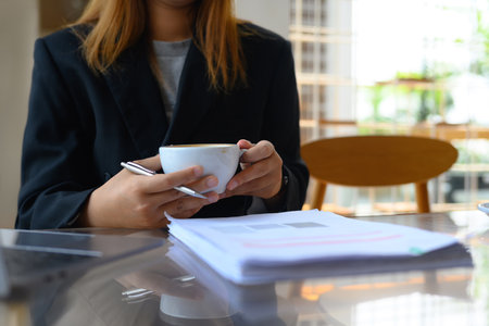 Young female manager holding coffee cup and working with document at desk.の写真素材