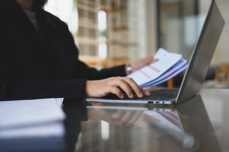 Young businessman in black suit checking financial reports at modern workplace.の写真素材