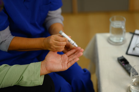 Medical worker using lancet on finger to checking blood sugar level senior patient at home.の写真素材