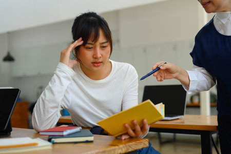 Mature lecturer helping female student struggling with schoolwork in a classroom.の写真素材