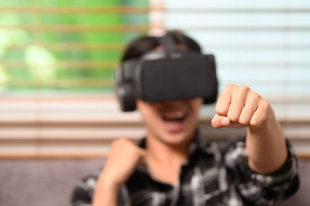 Joyful young man playing boxing game on virtual reality headset at home.の写真素材