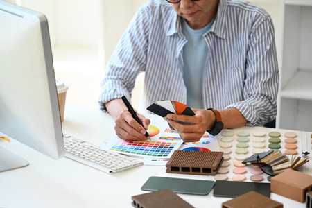 Experienced interior designer choosing paint tone from color swatch samples at desk.の写真素材