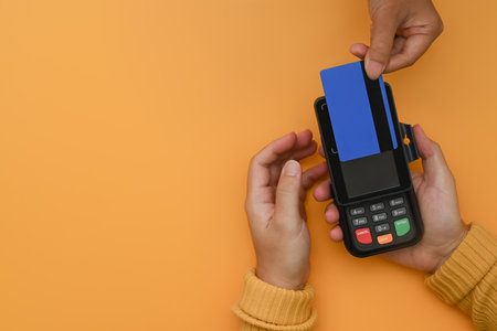 Overhead view of customer paying with cashless technology with credit card on yellow background.