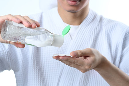 Man applying toner on cotton pad on white background. Male beauty and skincare concept.の写真素材