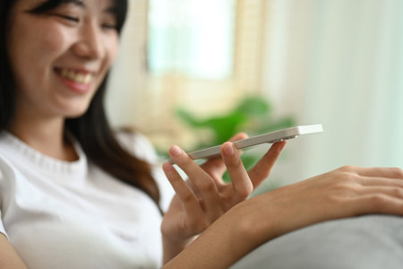 Smiling young woman in casual clothes enjoying pleasant mobile conversation in living room.の写真素材