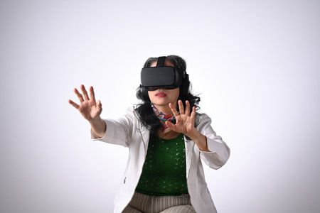 Excited middle age woman wearing VR headset and trying to touch something on white background.の写真素材