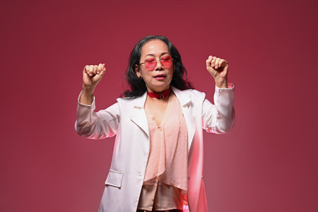 Happy senior woman in trendy glasses having fun dancing isolate on red background.の写真素材
