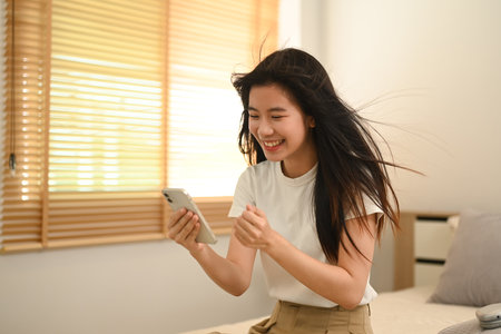 Young Asian woman reading text message on her phone with happy pleased face expression.の写真素材