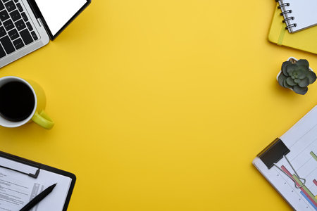 Laptop, financial reports and potted plant on yellow background. Top view with copy space.