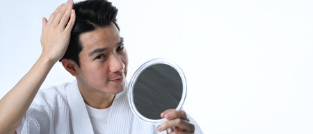 Young Asian man examining his hair while looking at the mirror isolated on white background.の写真素材
