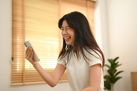 Joyful young Asian woman laughing while looking at smartphone.の写真素材