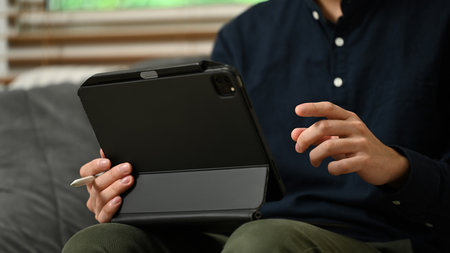 Close up young businessman sitting on sofa at home and using digital tablet.