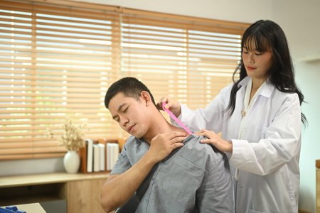Physical therapist putting kinesio tape on injured man shoulder. Rehabilitation and recovery concept.の写真素材