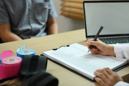 Physiotherapist having appointment with patient filling medical form at desk in rehabilitation center.の写真素材