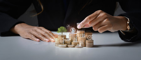 Businessman putting coin on stack with growing small tree symbolizing investment growth and saving...