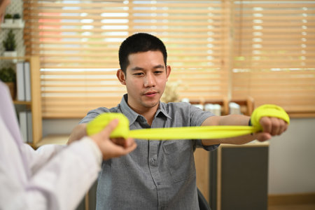 Male patient doing exercise with elastic bands at physiotherapy clinic. Rehabilitation and health care concept.の写真素材