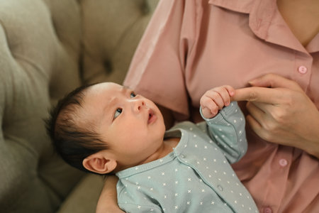 Cute sweet newborn baby lying comfortably in the mother arms, gazes up with curiosity. Motherhood...