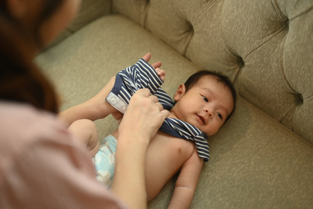 Shot of mother dressing her newborn baby lying on a comfortable couch. Motherhood concept.の写真素材