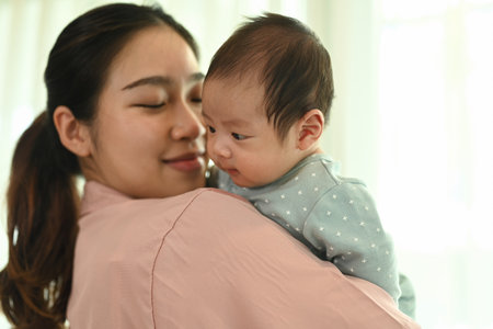 Loving Asian mother carrying her cute newborn baby at home. Childcare and motherhood concept.
