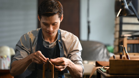 Focused craftsman meticulously stitching leather with a needle and thread. Leather craft concept.