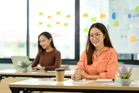 Portrait of smiling businesswoman sitting in an office with her colleagues in the background.の写真素材