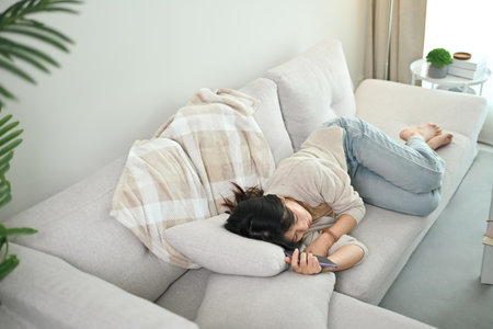 Asian young woman felling asleep on couch while hand holding mobile phone.の写真素材