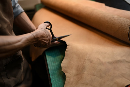 Close up an unrecognizable craftsman cutting leather with scissors at table.の写真素材