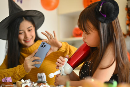 Happy mother and cute girl daughter having fun at home, preparing Halloween desserts in kitchen.の写真素材