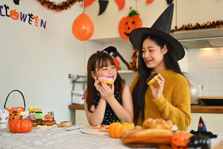 Happy mother and daughter dressed in Halloween costumes decorating cupcakes together in decorated kitchen.の写真素材