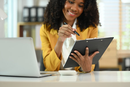 Pleased African American businesswoman analyzing stock market information on office table.の写真素材