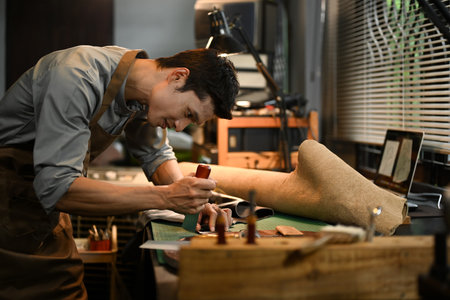 Focused male tailor cutting brown leather patterns in atelier workshop. Handmade concept.の写真素材
