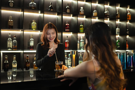 Pretty female bartender standing behind a bar counter serving drink to customer.の写真素材