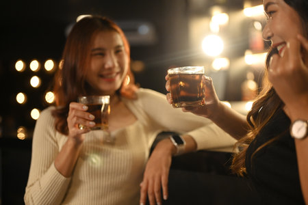 Two happy beautiful women enjoying drinks together in a cozy, dimly lit bar. Nightlife, celebrations and friendship concept.の写真素材